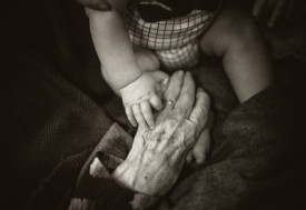 A great-grandmothers' hand reaching out to share a moment with her great grandson by Rod Long